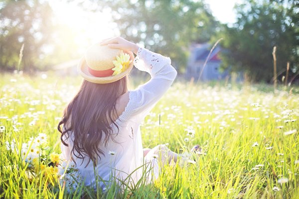 Junge Frau mit Sonnenhut sitzt auf Gras der Sonne entgegen