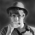 Junger Mann mit Hut spielt diatonische Mundharmonika